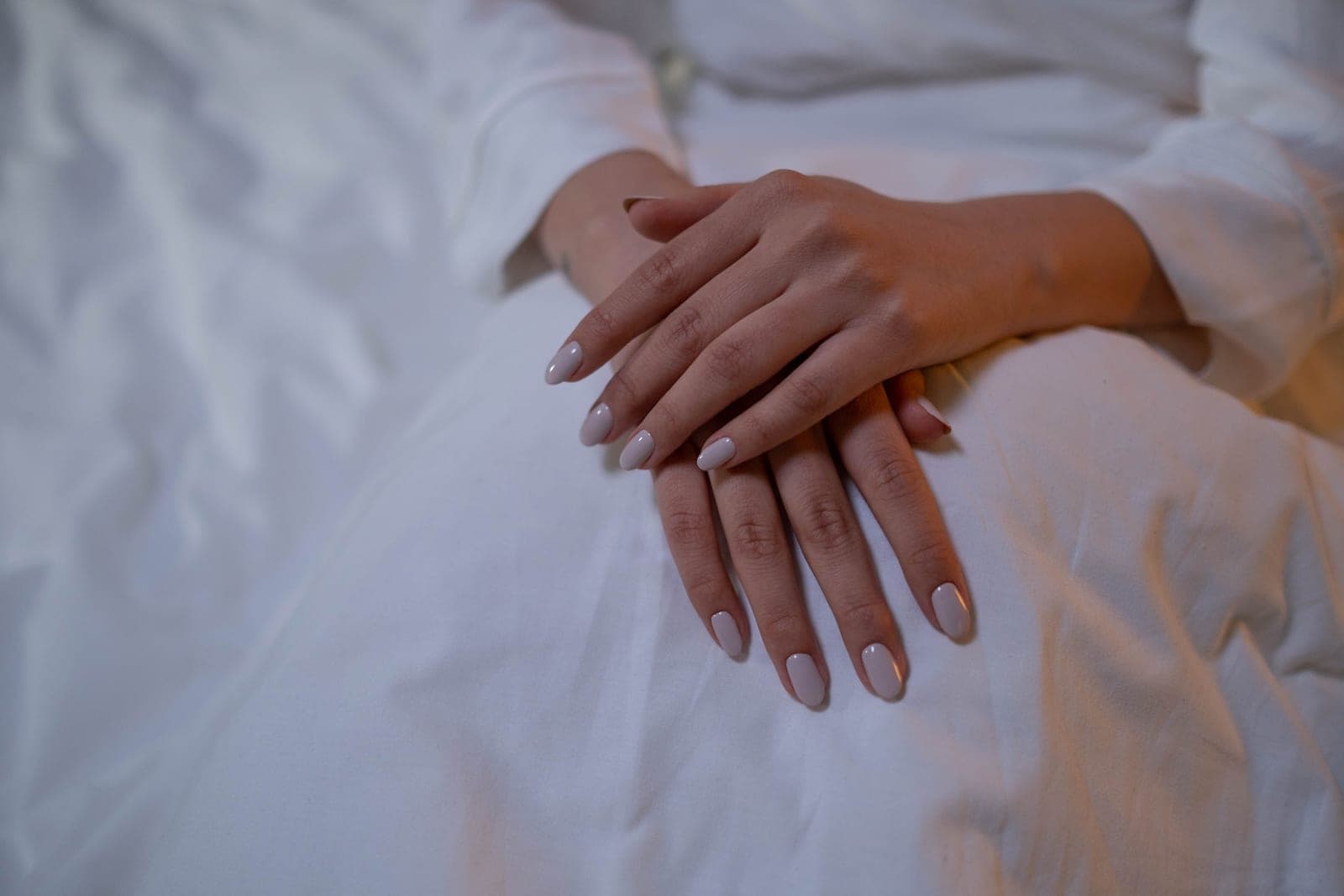 Short almond-shaped nude nails photographed close up in natural light